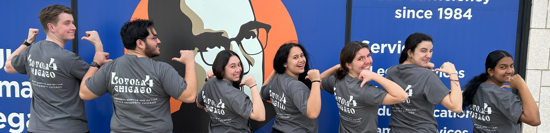 A group of volunteers with their backs to the camera pointing at their gray t-shirts